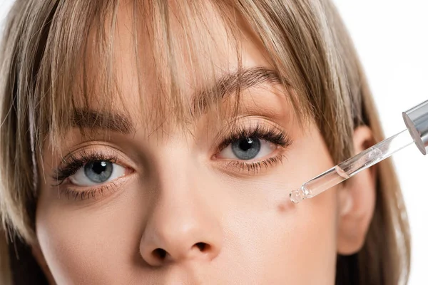 young woman with bangs applying serum isolated on white